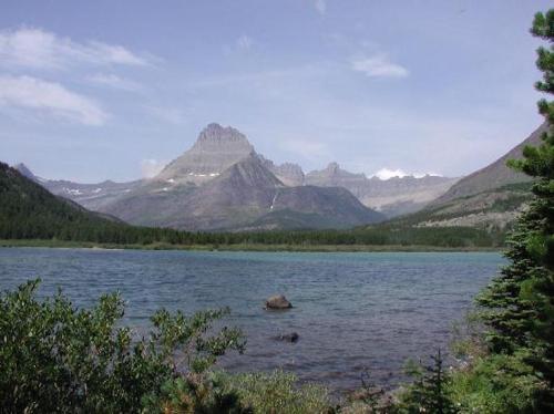 Scenic view of a mountain range with a clear lake in the foreground and lush greenery along the shore.