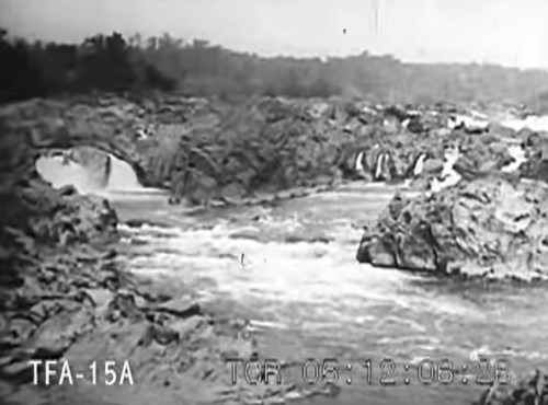 A rocky river landscape with flowing water and small waterfalls, surrounded by trees in the background.