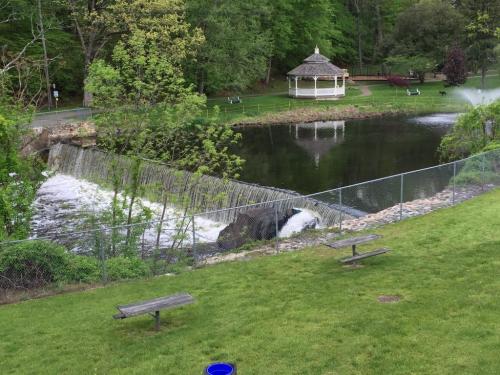 A serene park scene featuring a small waterfall, a pond, and a gazebo surrounded by greenery and picnic tables.