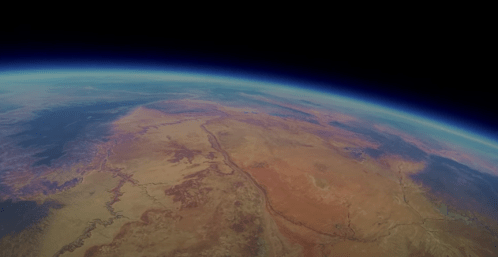 A view of Earth from space, showcasing a vast landscape of deserts and mountains beneath a blue atmosphere.