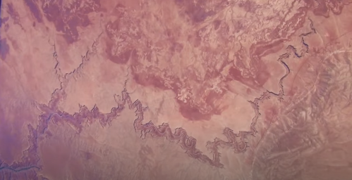 Aerial view of a rugged landscape with winding river patterns and varied terrain in warm tones.