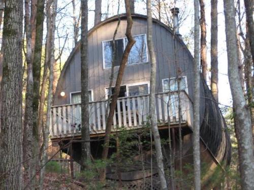 A unique, round wooden house elevated on stilts, surrounded by trees in a forested area.