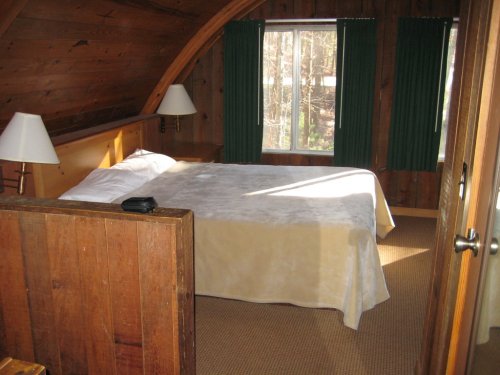 Cozy wooden bedroom with a large bed, two lamps, and green curtains, featuring natural light from a window.