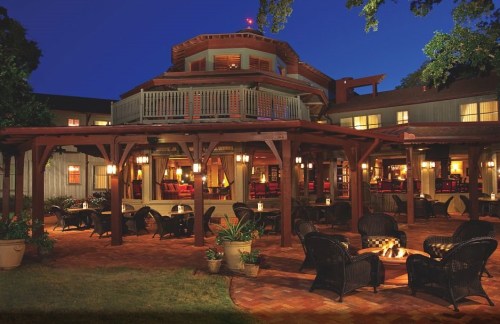 A cozy outdoor seating area with wicker chairs and a fire pit, illuminated at night near a charming building.