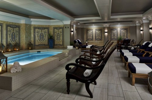 A serene spa interior featuring a hot tub, lounge chairs, and elegant decor with patterned walls and soft lighting.