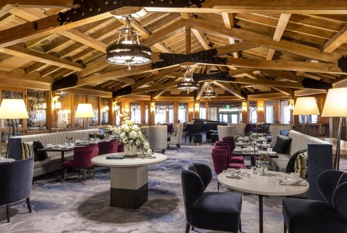Elegant restaurant interior with wooden beams, plush seating, and floral centerpieces, creating a warm ambiance.