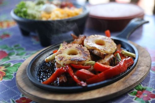 Sizzling dish on a wooden platter with grilled chicken, bell peppers, and pineapple slices, served on a colorful tablecloth.