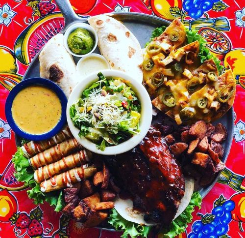 A vibrant platter of ribs, tortillas, salad, cheesy nachos, and crispy potatoes on a colorful tablecloth.