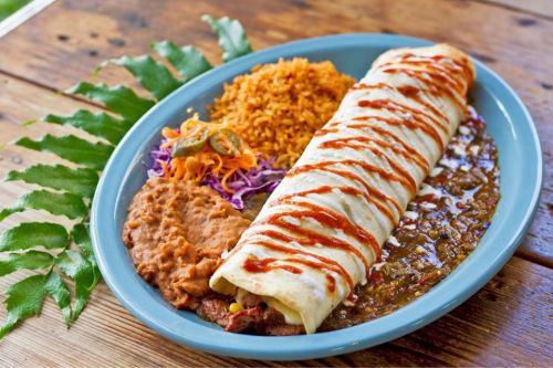 A plate of enchiladas topped with sauce, served with rice, refried beans, and a side of colorful slaw.