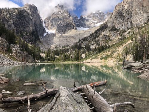 A serene mountain lake surrounded by rocky cliffs and lush greenery, reflecting the sky and clouds above.