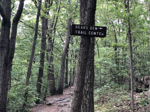 A wooden sign points to "Bears Den" and "Trail Center" along a wooded hiking path surrounded by trees.