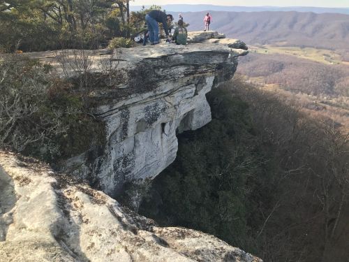 A group of hikers on a rocky cliff overlooking a valley with mountains in the background.