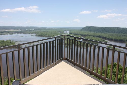 A scenic view from a balcony overlooking a river and lush green landscape under a clear blue sky.