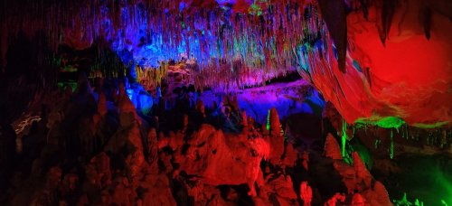 A colorful cave interior with vibrant stalactites and stalagmites illuminated in shades of blue, purple, red, and green.
