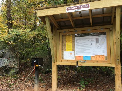 Information kiosk at a trailhead, featuring maps and notices, surrounded by trees and rocky terrain.
