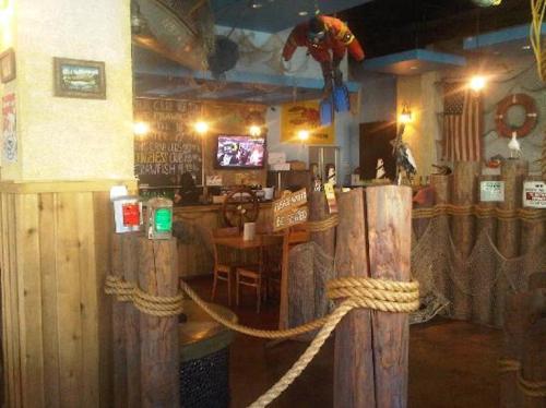 Interior of a themed restaurant with nautical decor, wooden beams, and a suspended figure, featuring tables and a TV.