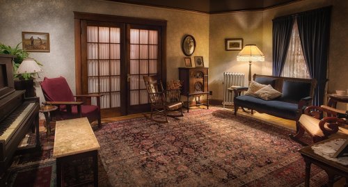 Cozy vintage living room with a piano, armchairs, a sofa, and warm lighting, featuring a patterned rug and decorative accents.