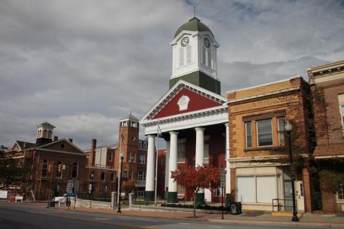 Historic building with a clock tower, red facade, and white columns, set against a cloudy sky.