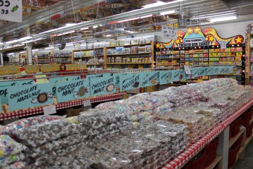 A colorful candy store display with various candy types in bins and shelves, featuring signs for chocolate options.