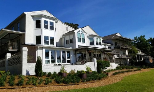 A row of modern, multi-story houses with large windows, surrounded by green grass and landscaping under a clear blue sky.