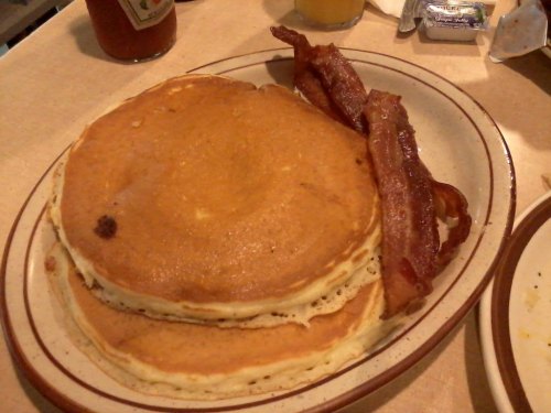 A plate with two fluffy pancakes and crispy bacon strips on the side.