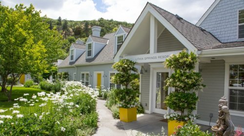 A charming resort with a landscaped garden, featuring blooming flowers and a welcoming entrance under a sunny sky.