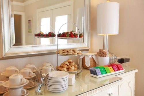 A tiered stand with pastries and strawberries beside a coffee setup and colorful tea boxes on a table.