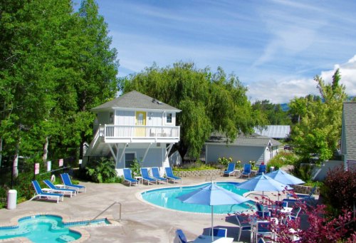 A sunny pool area with lounge chairs, umbrellas, and a small building surrounded by trees.