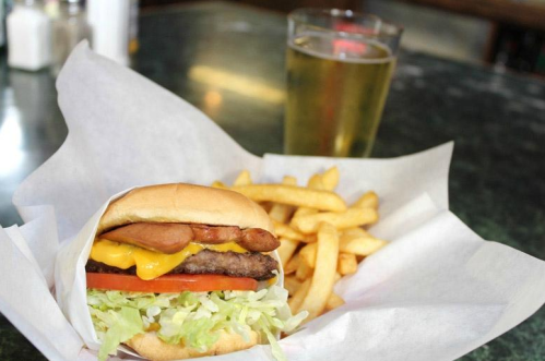 A juicy cheeseburger with lettuce, tomato, and bacon, served with fries and a glass of beer on a table.