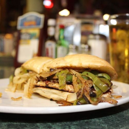 A close-up of a sandwich filled with grilled chicken, sautéed onions, and green peppers on a plate.