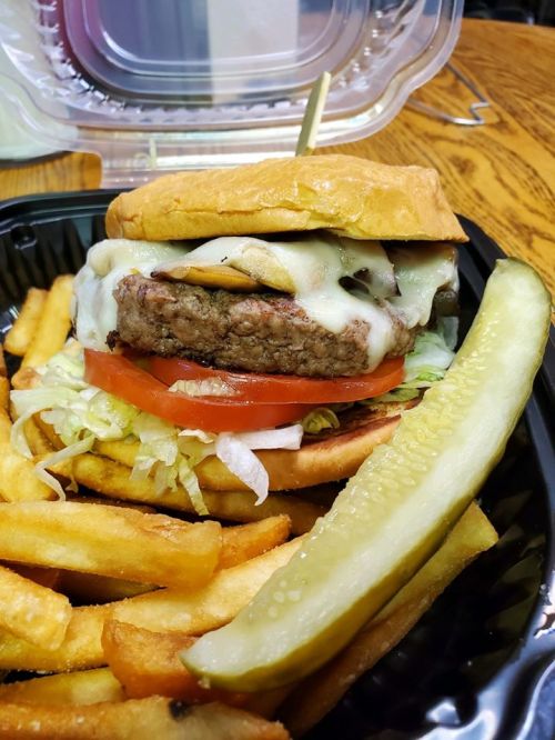A juicy cheeseburger with lettuce, tomato, and pickles, served with crispy fries in a takeout container.