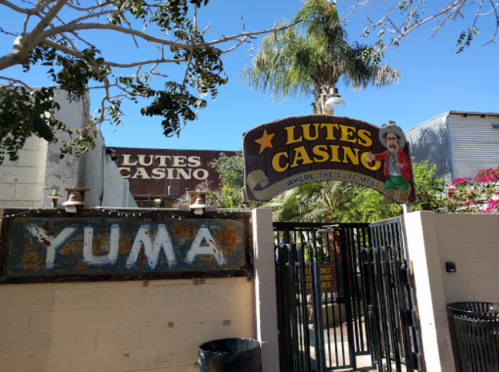 Entrance to Lutes Casino in Yuma, featuring a colorful sign and palm trees under a clear blue sky.