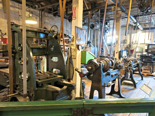A vintage workshop filled with old machinery, including lathes and milling machines, in a well-lit industrial space.