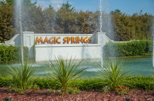 Sign for Magic Springs amusement park with water fountains and greenery in the background.
