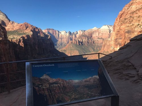 A scenic view of a canyon with a sign labeled "Canyon Overlook" in the foreground, showcasing the stunning landscape.