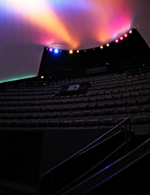 Interior of a theater with colorful lights illuminating a curved ceiling and empty seating.