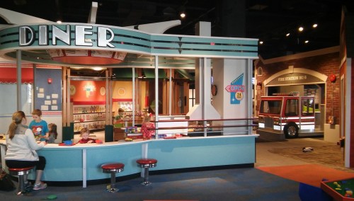 A colorful children's play area featuring a diner, fire truck, and kids playing with toys.