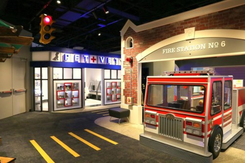 A colorful play area featuring a fire station and a pet vet clinic, with a toy fire truck and traffic lights.