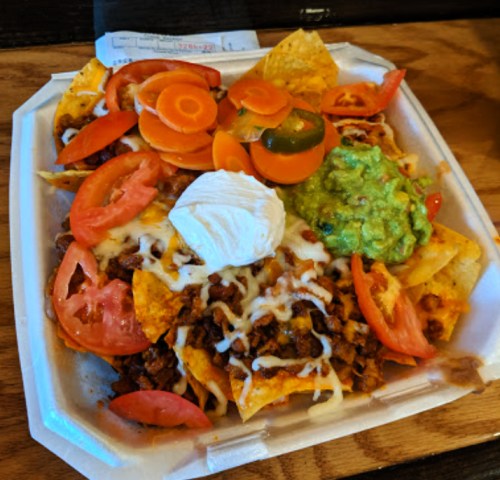 A plate of nachos topped with ground beef, cheese, tomatoes, jalapeños, guacamole, sour cream, and sliced carrots.
