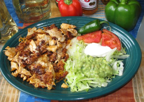 A plate of seasoned chicken with lettuce, guacamole, tomato, and sour cream, surrounded by colorful peppers.