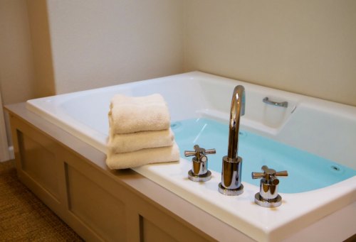 A modern bathtub with a light blue interior, featuring stacked white towels and stylish chrome faucets.