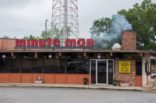 A restaurant named "minute man" with a brick exterior, smoke rising from a chimney, and colorful decorations outside.