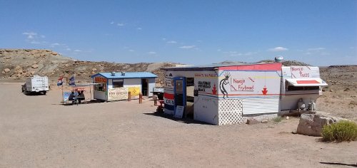 Two food trucks in a desert landscape, one serving fry bread and the other tacos, with a clear blue sky above.