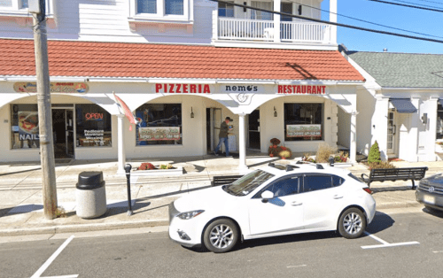 A white car parked in front of a pizzeria and restaurant with a red awning and "OPEN" sign.