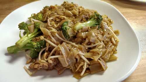 A plate of stir-fried noodles with broccoli, bean sprouts, and pieces of meat in a savory sauce.