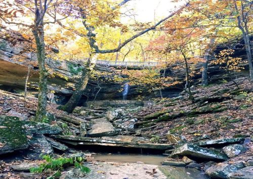 A serene canyon scene with autumn foliage, a small waterfall, and rocky terrain under a clear sky.