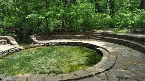 A circular stone pool surrounded by lush green trees in a natural setting, labeled "Buffalo Springs."