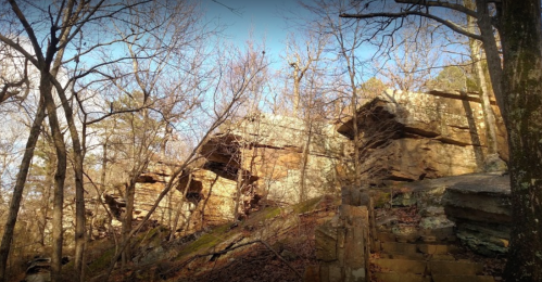 Rocky outcrops surrounded by bare trees and underbrush, illuminated by soft sunlight in a natural setting.
