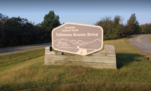 Sign for Talimena Scenic Drive in Ouachita National Forest, Oklahoma, surrounded by grass and trees.