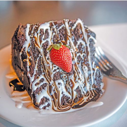A slice of chocolate cake drizzled with white and dark chocolate sauce, topped with a fresh strawberry.